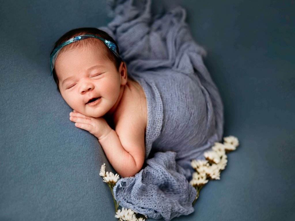 baby posed on a blue blanket with her little hands under her chin, this is part of a workflow of newborn posing the nest step is to pose the newborn baby into the bum up pose 